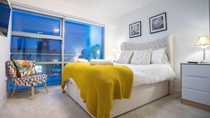 A bedroom with a bed, a chair, a desk, and a window with a view. - Live in Leeds Millenium Square Apartment (Leeds)