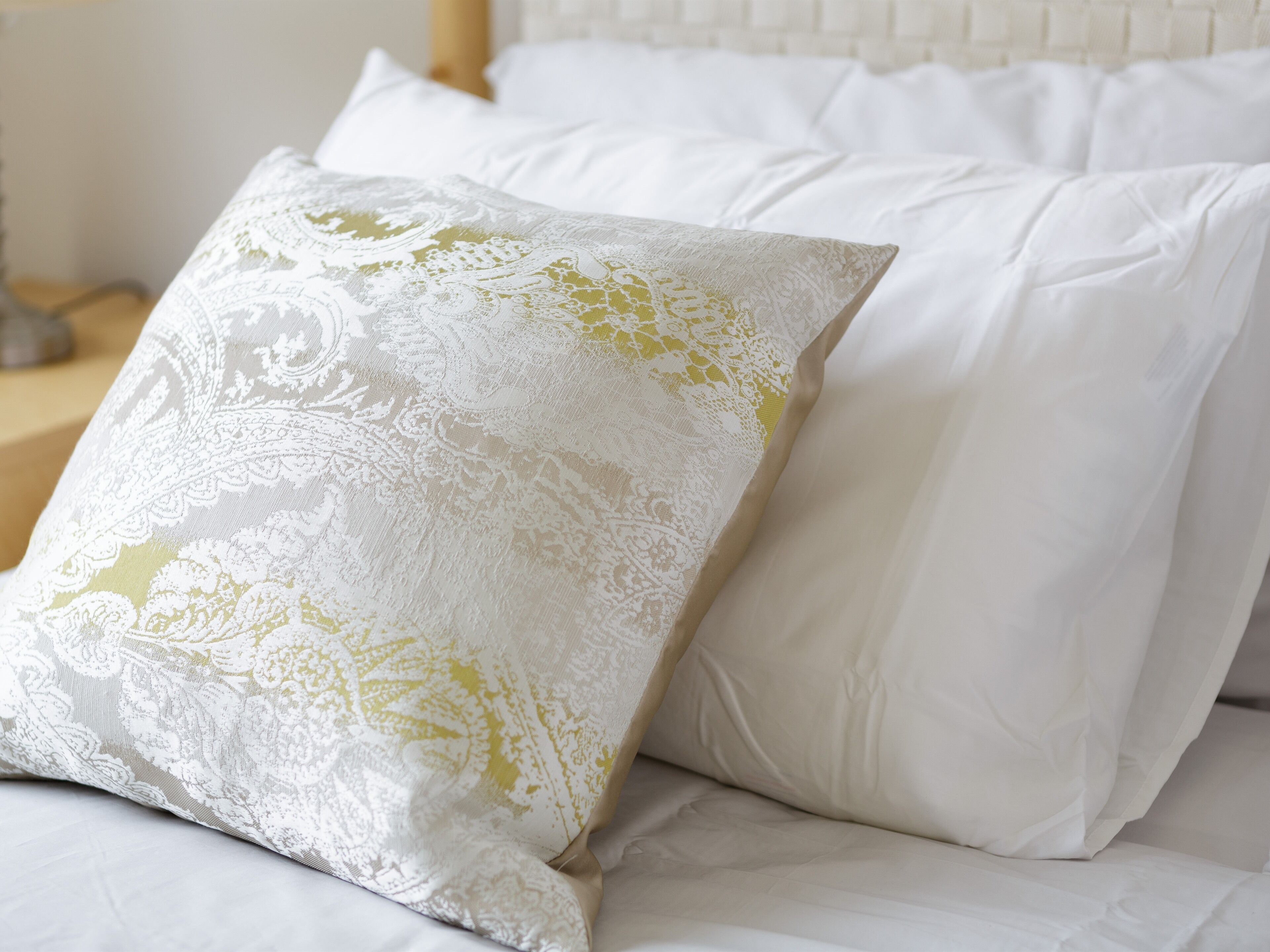 A bed with white bedding and a decorative pillow with a floral pattern.