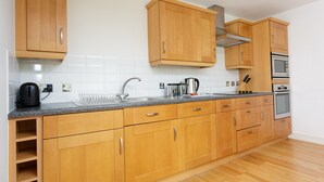 A kitchen with wooden cabinets, a granite countertop, a stainless steel sink, a kettle, and two ovens. - Live in Leeds Millenium Square Apartment (Leeds)
