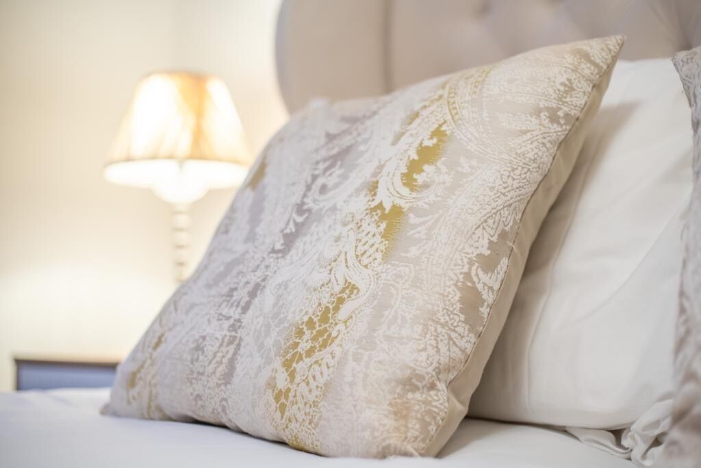 A bed with a white pillow and a decorative pillow with lace detailing.