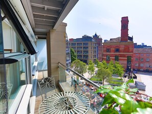 A balcony with a glass railing overlooking a cityscape, featuring historic buildings and a clear sky.