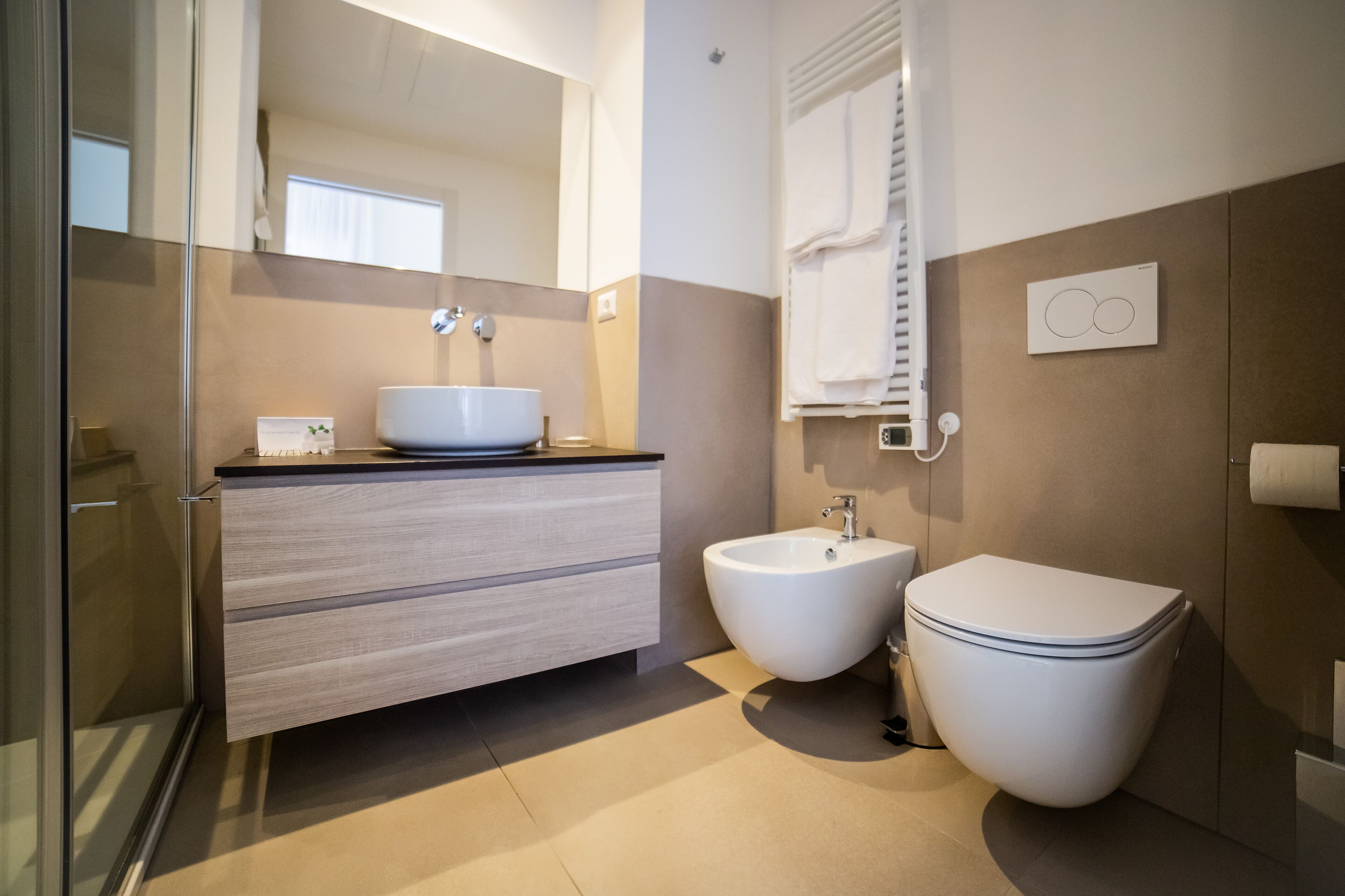 Een moderne badkamer met een douchecabine van glas, een witte wastafel, een toilet en een hygiëneschuiver.