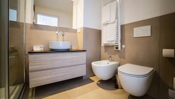 Een moderne badkamer met een douchecabine van glas, een witte wastafel, een toilet en een hygiëneschuiver.