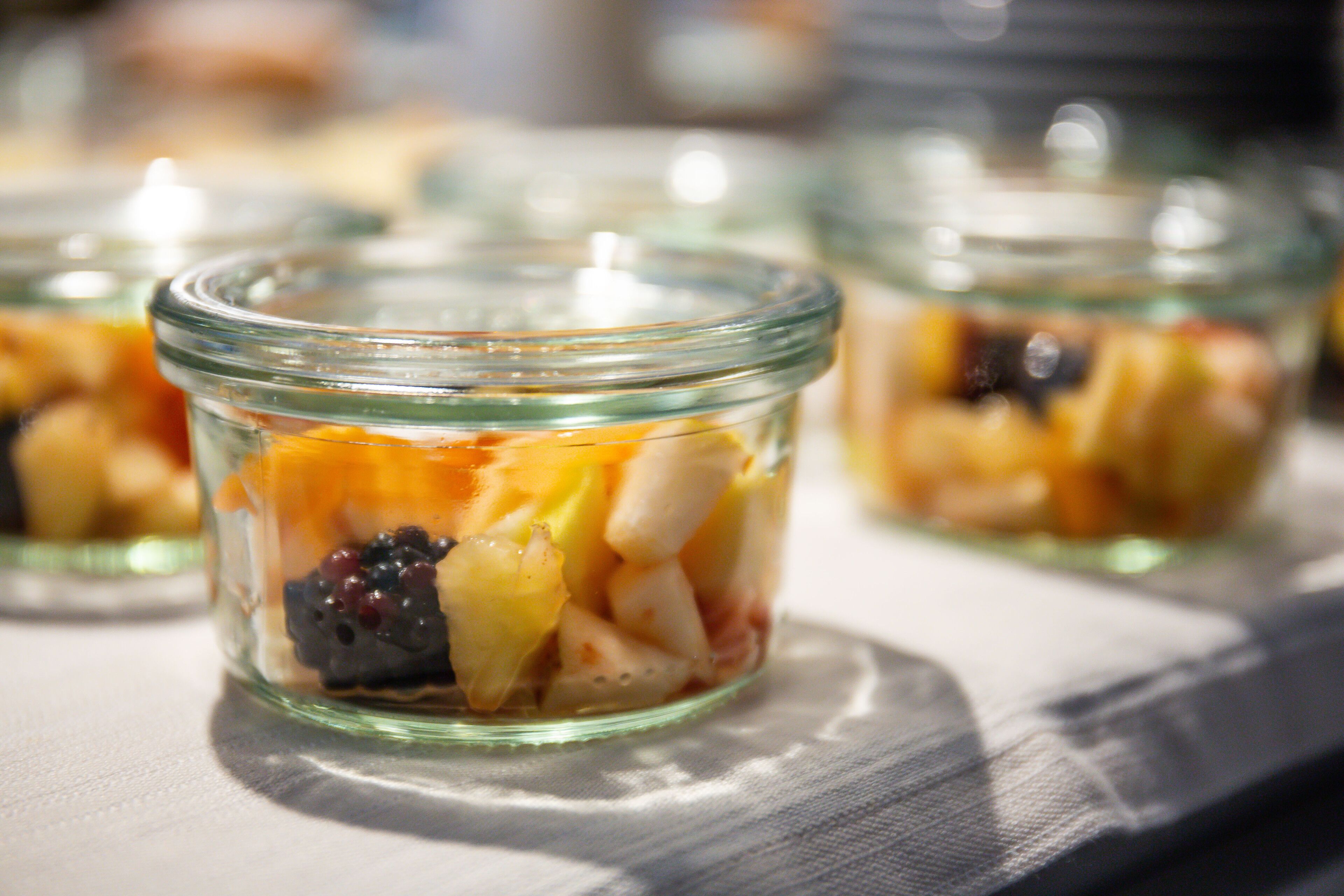 Une vue rapprochée d’un bocal en verre contenant une salade de fruits composée de différents fruits.
