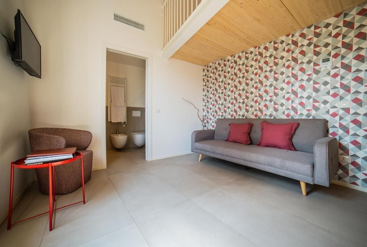 Ein modernes Wohnzimmer mit einer grauen Couch, roten Kissen, einem roten Metall-Beistelltisch und einer Wand mit Muster.