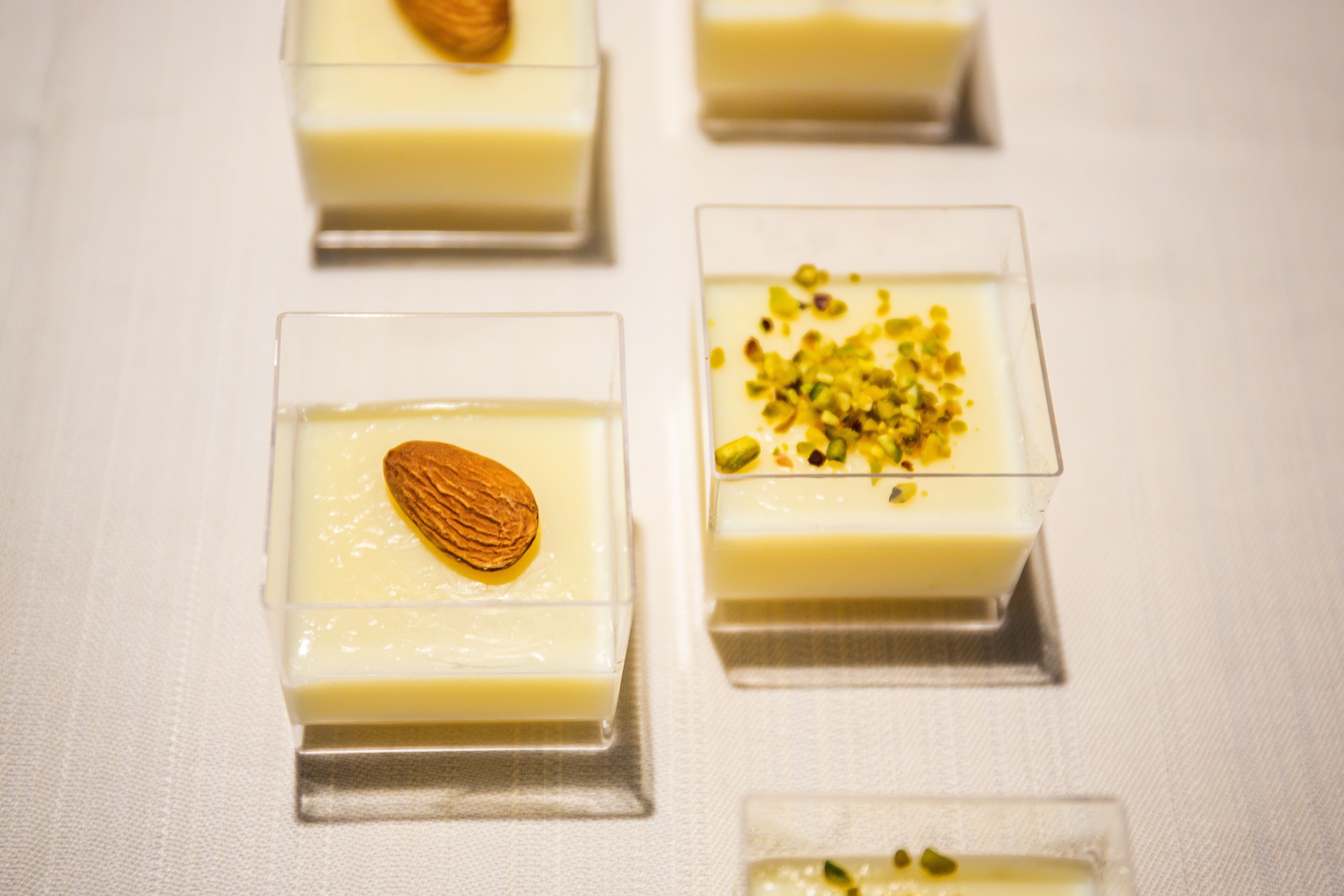 Four square glass dessert dishes with a creamy white filling, one topped with an almond and another with pistachios.