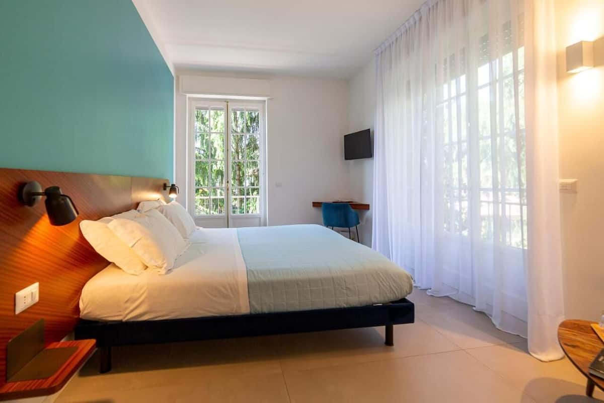 Un dormitorio con cama, escritorio, silla, televisor y ventana con cortinas.