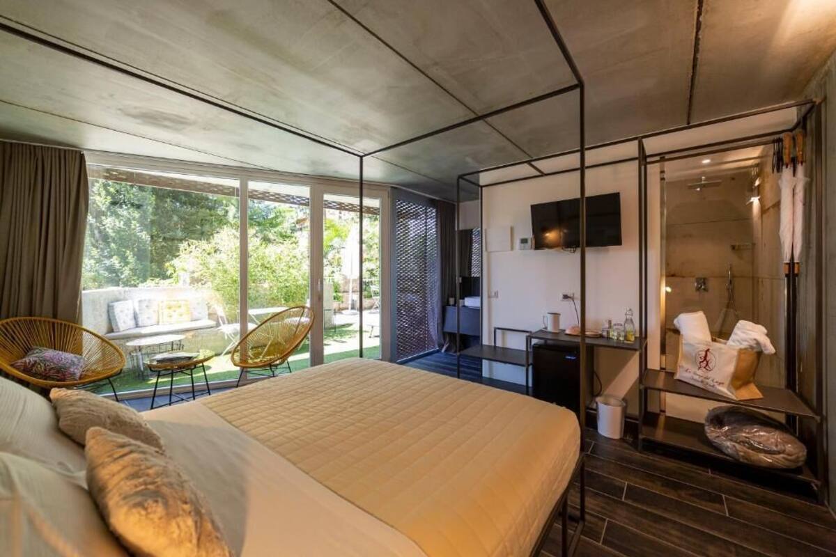Habitación de hotel moderna con una cama grande, televisión, baño con ducha y balcón con mobiliario exterior.