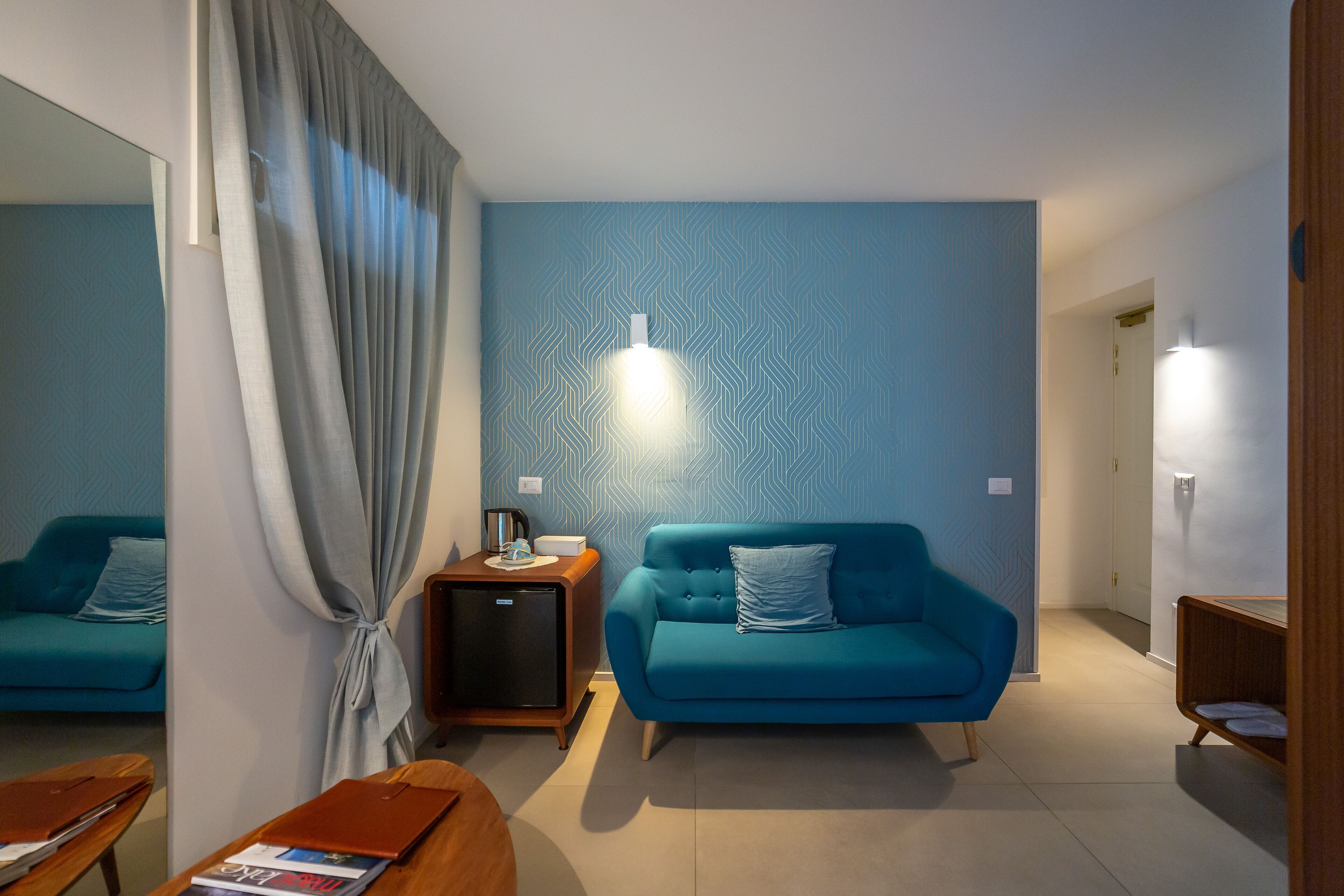 Un soggiorno moderno con un divano blu, un piccolo tavolino in legno, uno specchio e un faretto a parete.