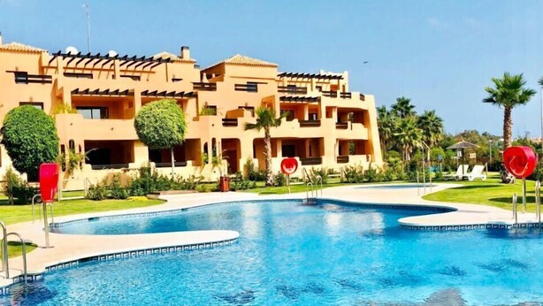 Un hotel con una grande piscina, palme e un cielo azzurro limpido.