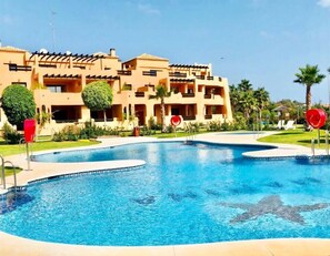 A hotel with a large swimming pool, palm trees, and a clear blue sky. - Casares Beach Golf Apartment With Private Garden and Pool Access (Casares)