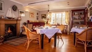 A cozy dining room with a fireplace, wicker chairs, and a table set for two. - Lochview Guesthouse (Strathpeffer)