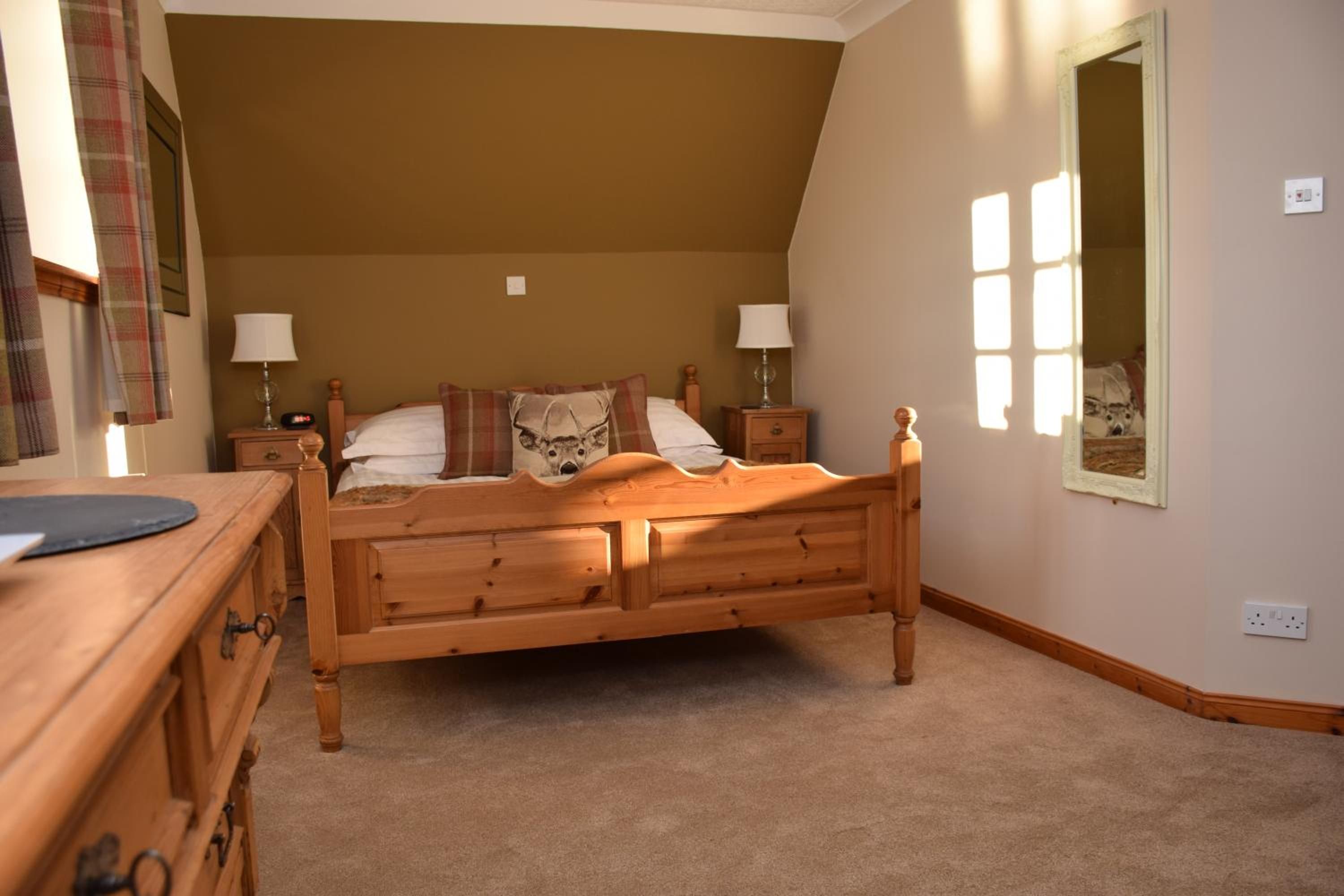 A bedroom with a wooden bed, two bedside tables, a nightstand, a dresser, and a window with daylight.