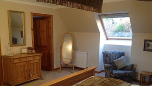A bedroom with a large bed, a wooden dresser, a mirror, a chair, and a window with a view of greenery. - Lochview Guesthouse (Strathpeffer)