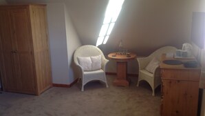 A room with a sloped ceiling, a wooden wardrobe, two wicker chairs, a small round table with a bottle, and a wooden dresser. - Lochview Guesthouse (Strathpeffer)