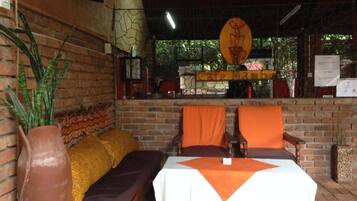 A rustic outdoor seating area with a brick wall, a cushioned bench, and a table with a white tablecloth.