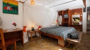 A cozy room with a bed, a desk, and a chair. There is a painting on the wall and a window with curtains. - Outpost Lodge (Arusha)