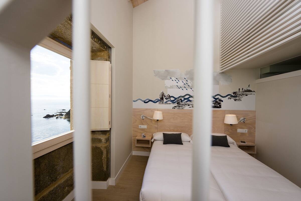 Ein Hotelzimmer mit Bett, Nachttischen, Wandgemälde und Meerblick.