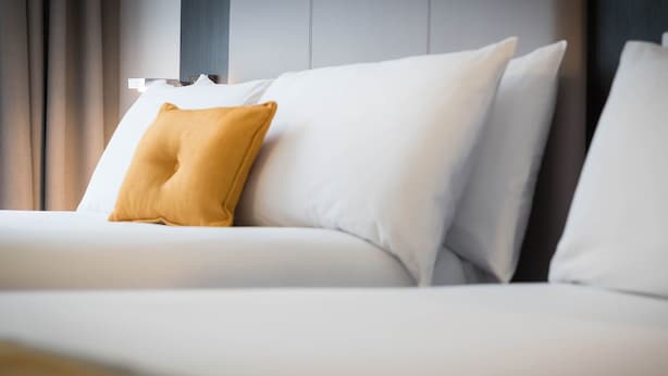 A modern hotel room with a neatly made bed, a single mustard-colored pillow, and a minimalist design. - Maldron Hotel South Mall Cork City (Cork)