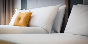 A modern hotel room with a neatly made bed, a single mustard-colored pillow, and a minimalist design. - Maldron Hotel South Mall Cork City (Cork)