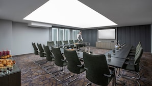 A conference room with a long table, multiple chairs, a projector screen, and a skylight. - Maldron Hotel South Mall Cork City (Cork)