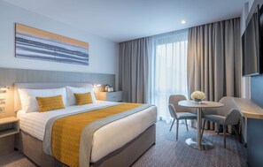 Habitación de hotel con una cama grande, un escritorio con dos sillas, una pequeña mesa con flores y un televisor en la pared.