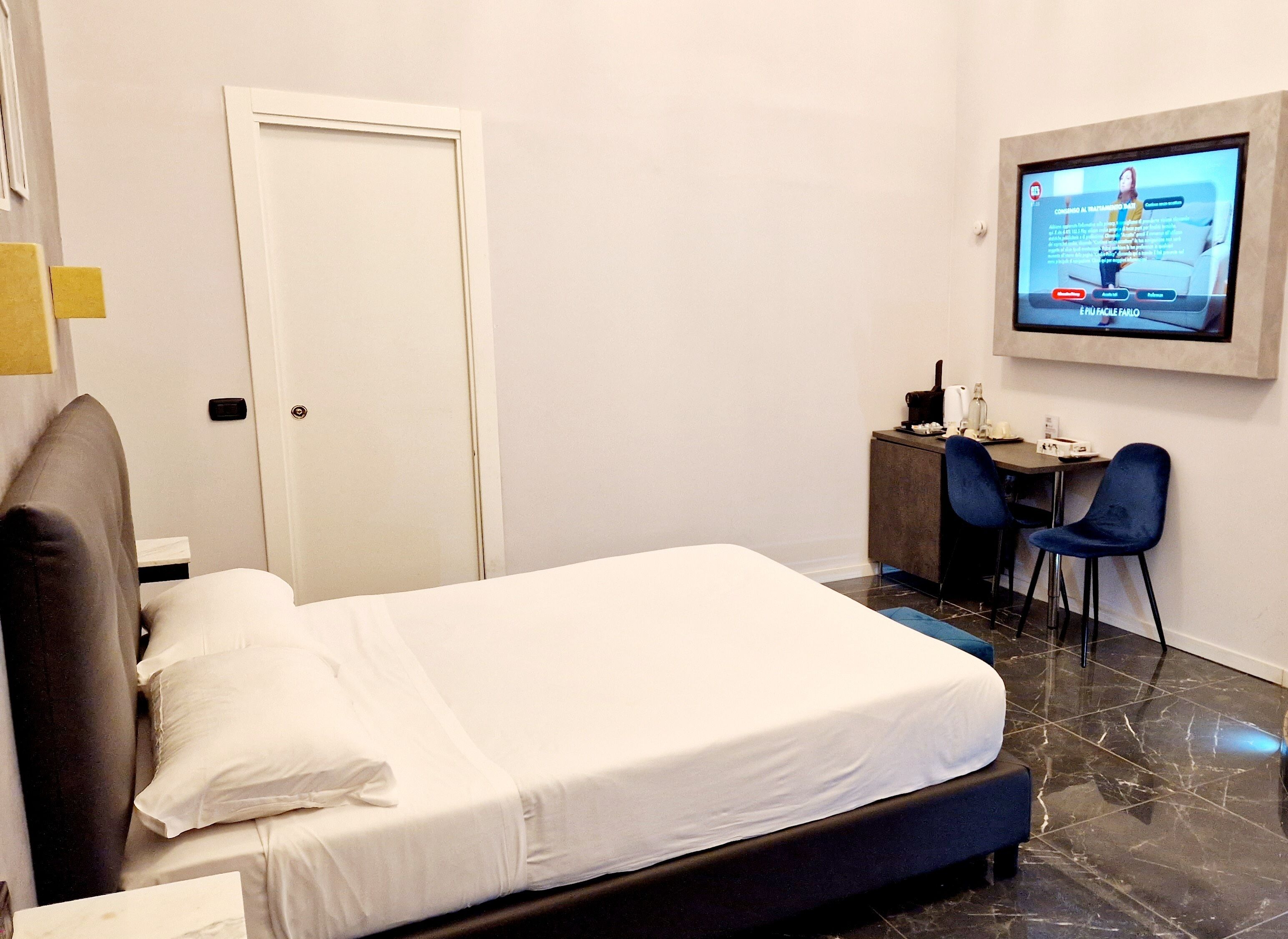A hotel room with a bed, a desk with two chairs, a television mounted on the wall, and a door.