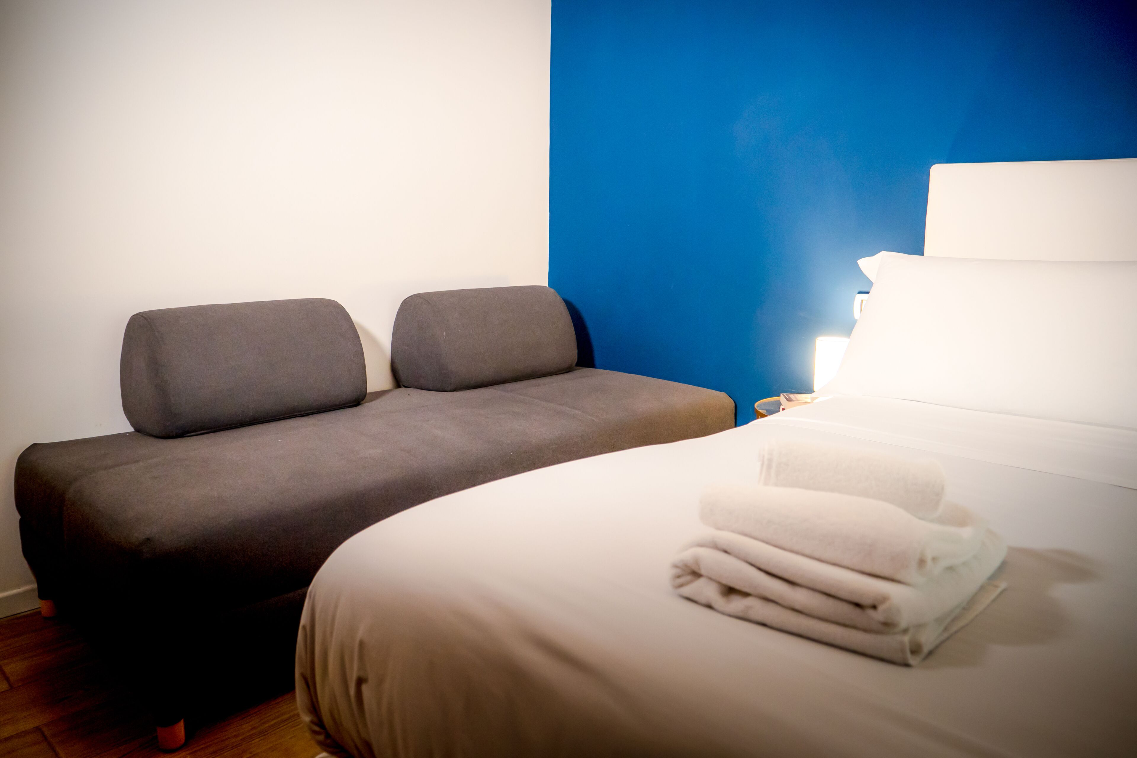 Una habitación con una cama, un sofá y una mesita de noche con lámpara.