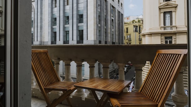 A balcony with two wooden chairs and a small table, overlooking a cityscape with historic buildings. - Comfort Zone Naples (Naples)
