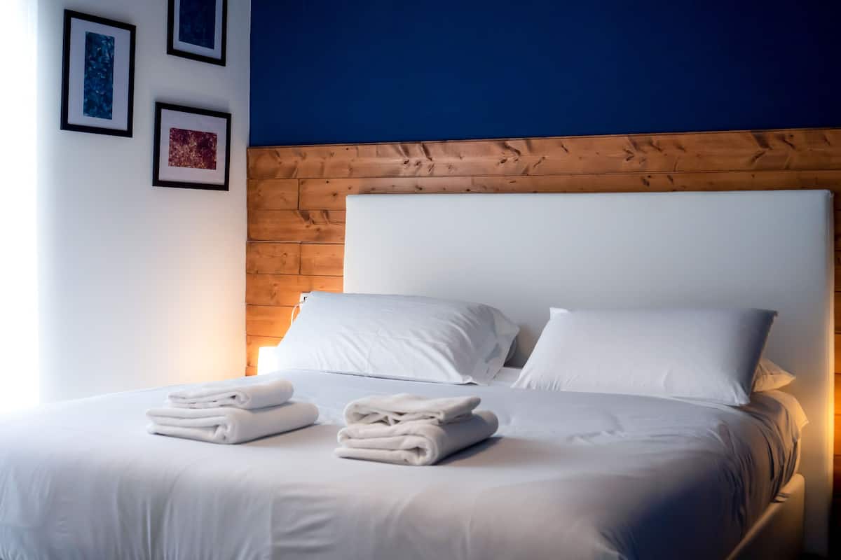 Una cama bien tendida con sábanas y toallas blancas, un cabecero de madera y cuadros en la pared.