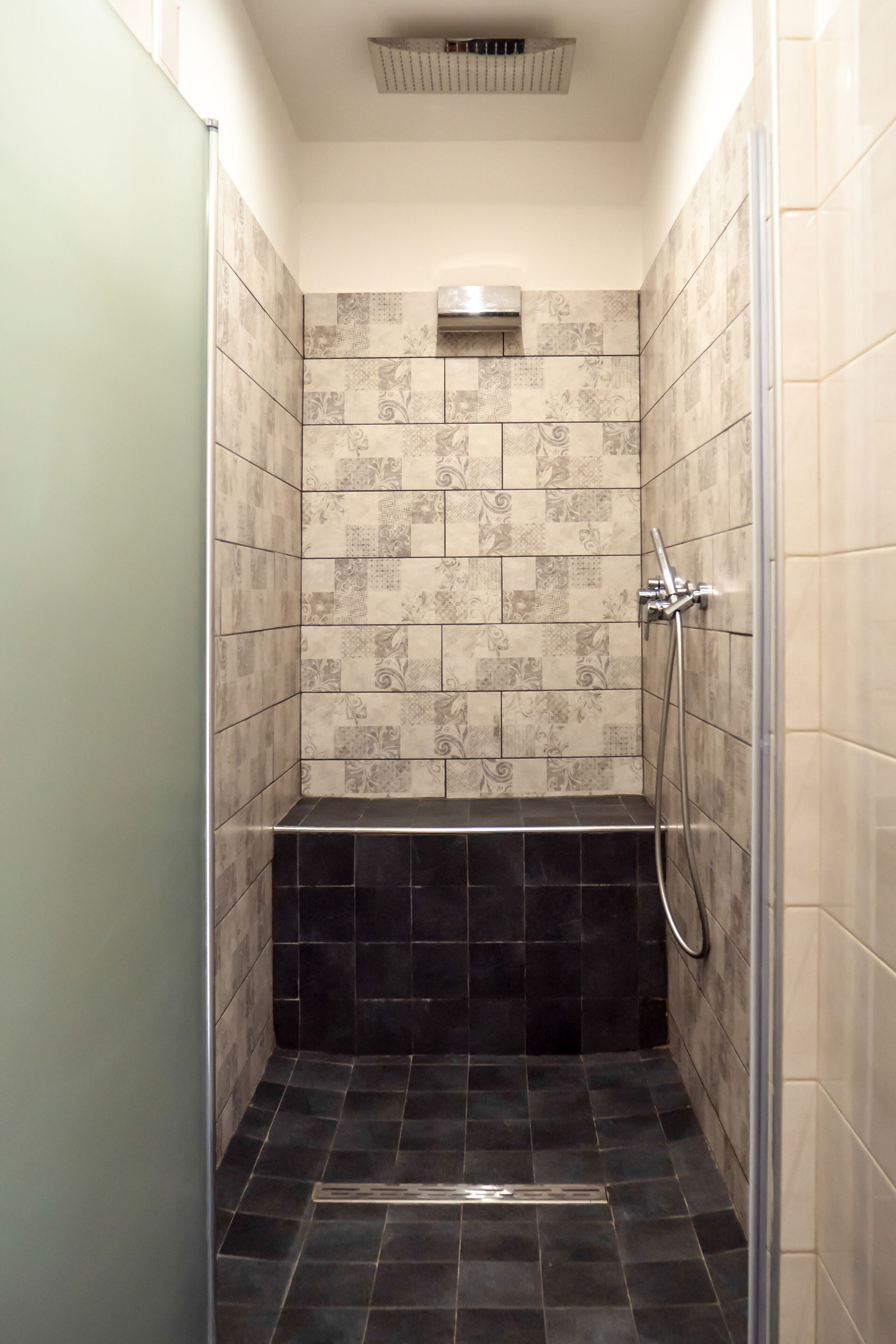 A small, enclosed shower area with patterned tiles and a black floor.