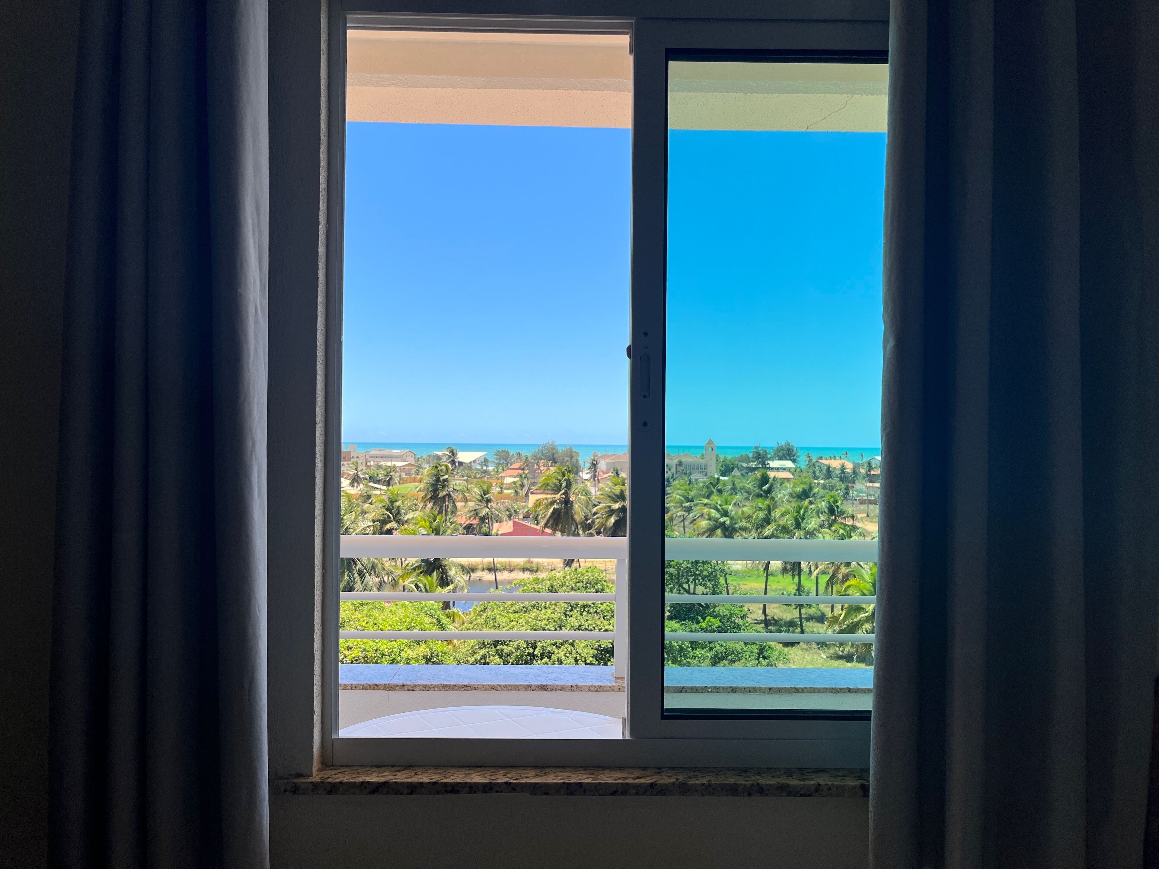 A balcony with a view of a coastal area, including buildings and palm trees.