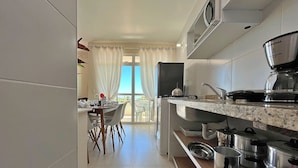 A modern kitchen with a dining area, large windows, and a view of the sea. - SAN GIACOMO I Apartamentos por temporada no Porto das Dunas (Aquiraz)