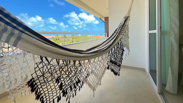 A hammock on a balcony with a view of the sky and buildings. - SAN GIACOMO I Apartamentos por temporada no Porto das Dunas (Aquiraz)