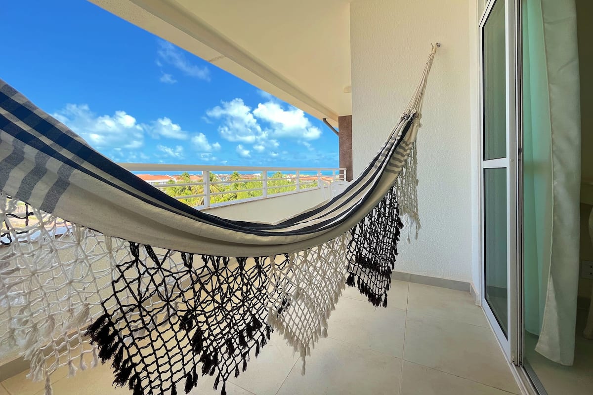 A hammock on a balcony with a view of the sky and buildings.