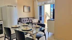 A dining area with a glass table set for four, a brown leather sofa, and a white cabinet. - SAN GIACOMO I Apartamentos por temporada no Porto das Dunas (Aquiraz)