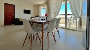 A dining area with a table set for four, a sofa, a TV, and a balcony with a view. - SAN GIACOMO I Apartamentos por temporada no Porto das Dunas (Aquiraz)