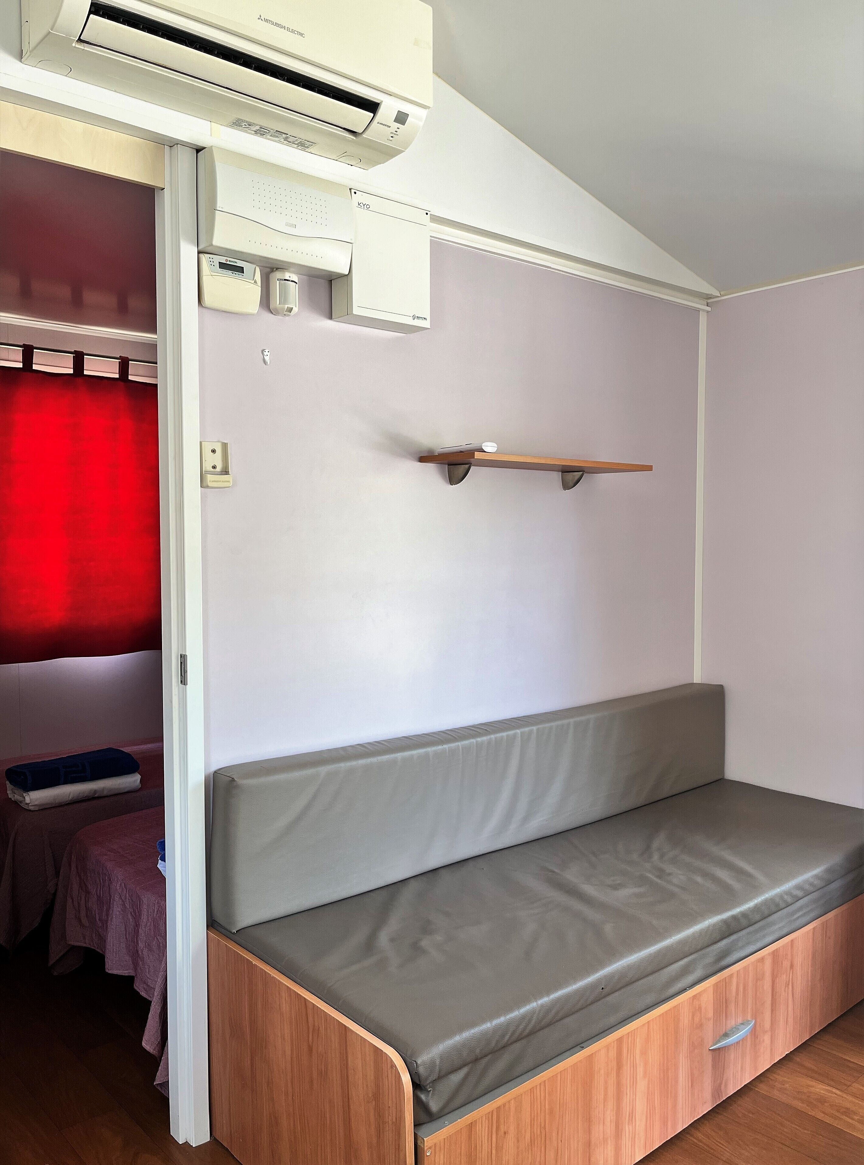 Una habitación compacta con un banco incorporado, un estante pequeño y un equipo de aire acondicionado.