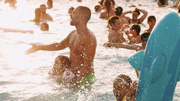 Ein überfüllter Pool im Freien, an dem sich Menschen im Wasser vergnügen.