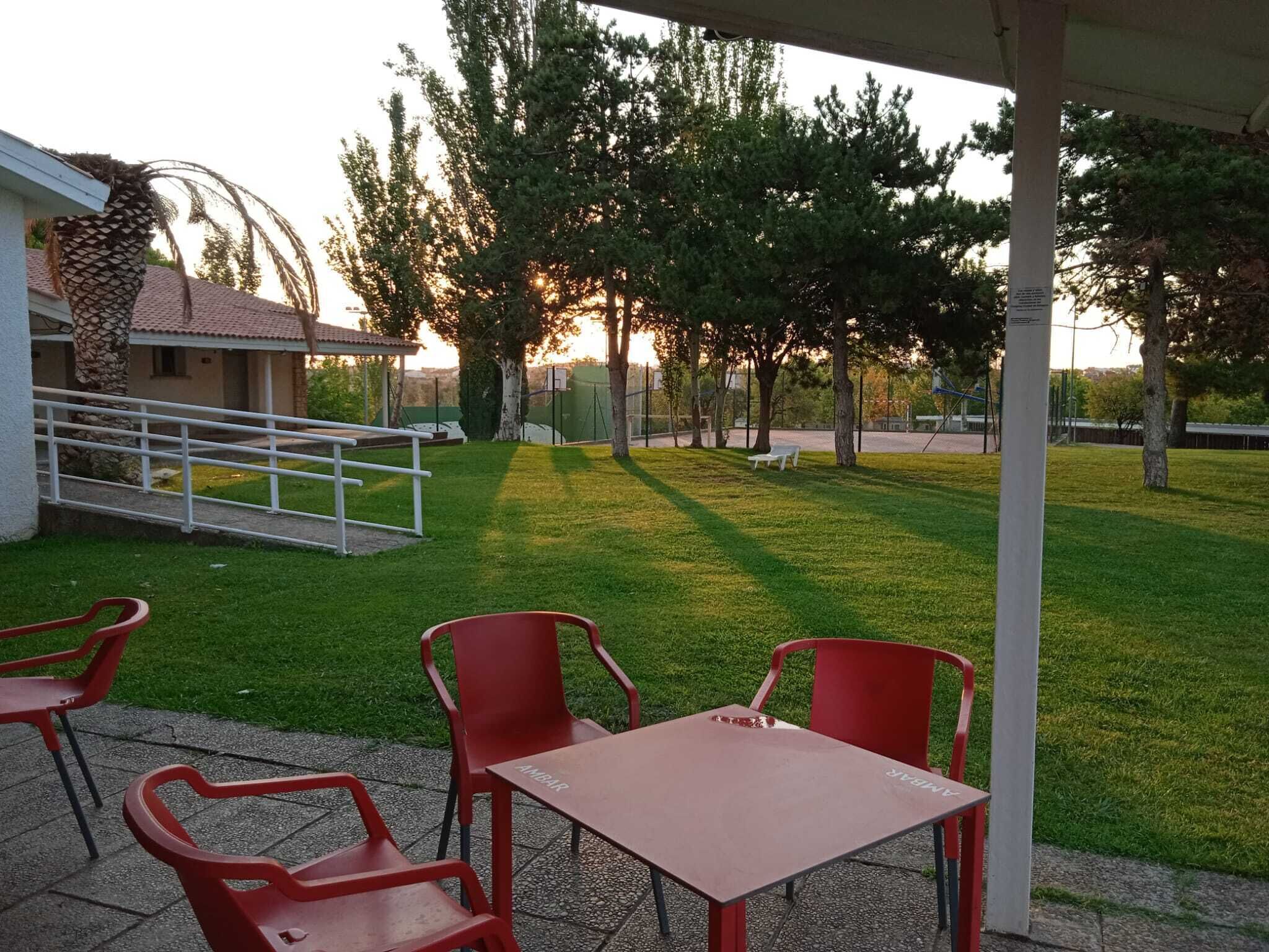 A patio area with a table and chairs, a covered seating area, and a view of trees and a building in the background.