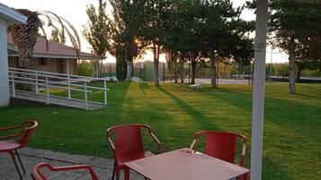 A patio area with a table and chairs, a covered seating area, and a view of trees and a building in the background.