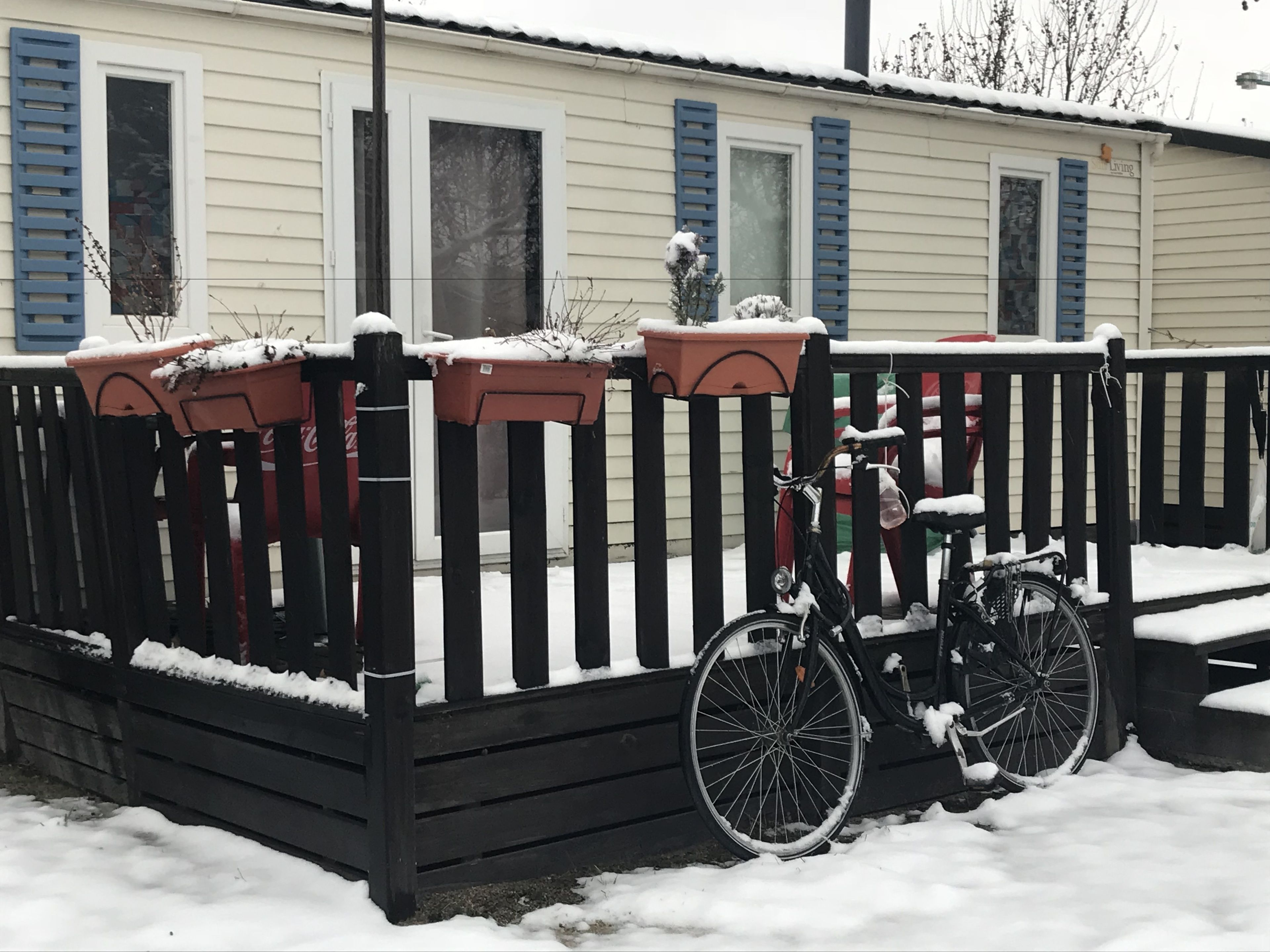 Un espace extérieur enneigé, avec un vélo garé près d’une clôture en bois.