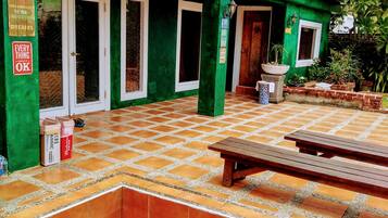 A green building with a tiled patio, a wooden bench, and a trash bin.