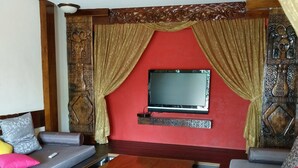 A living room with a wooden coffee table, two sofas, a flat-screen TV mounted on a red wall, and decorative curtains. - Land of joy Ubud Hall (Hengchun)