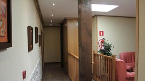 A hallway with wooden railings, framed pictures on the wall, a red fire extinguisher, and a pink chair. - Hostal Oianume (Urnieta)