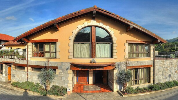 A two-story building with a stone facade, large windows, and a prominent arched entrance. - Hostal Oianume (Urnieta)