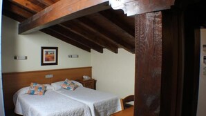 A room with two beds, wooden beams, a wooden headboard, a bedside table with a phone, and a framed picture on the wall. - Hostal Oianume (Urnieta)