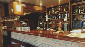 A bar with a brick counter, wooden stools, and shelves stocked with liquor bottles. - Hostal Oianume (Urnieta)