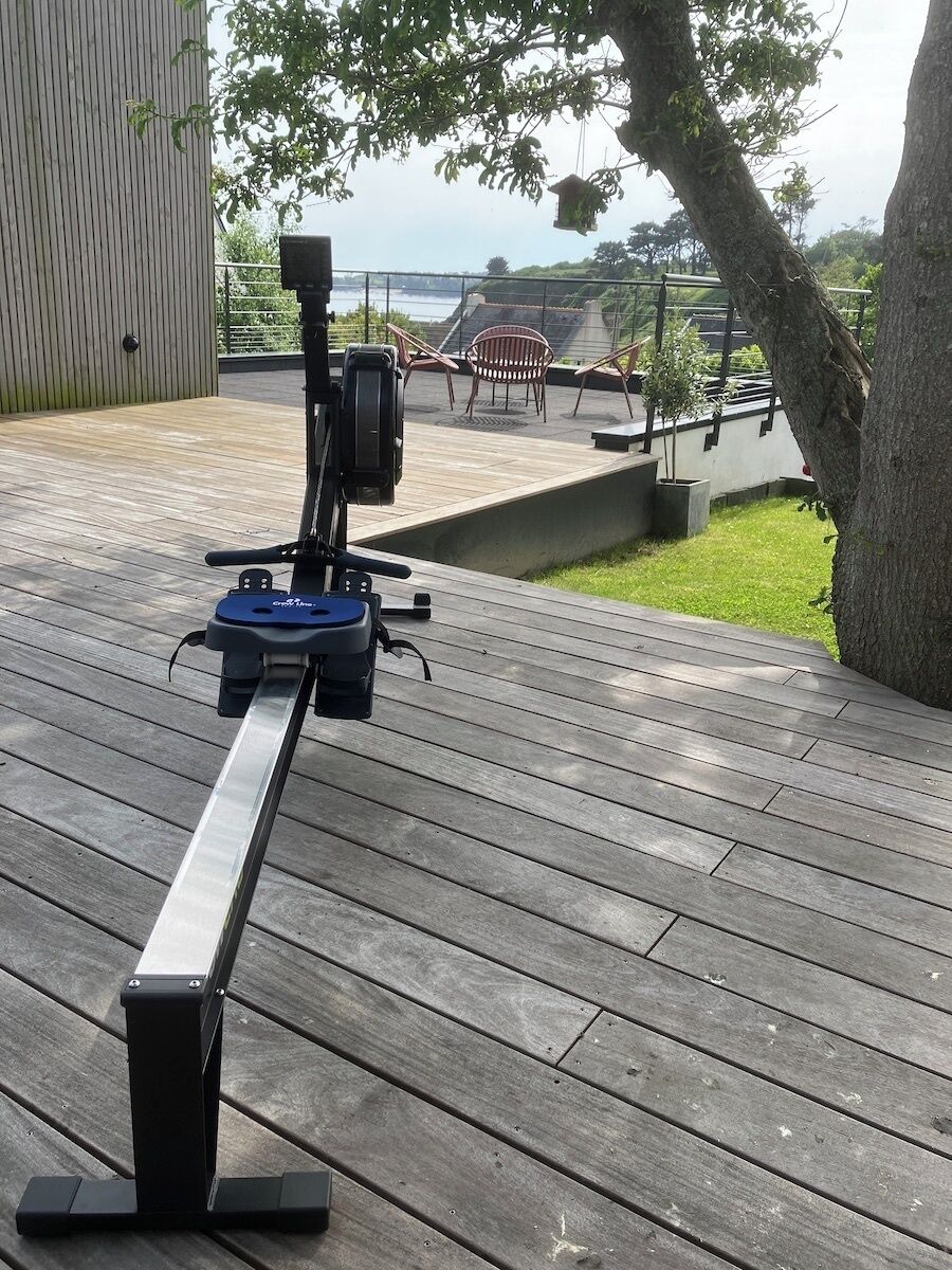 A deck with a stationary exercise bike, a railing, and a view of the sea.