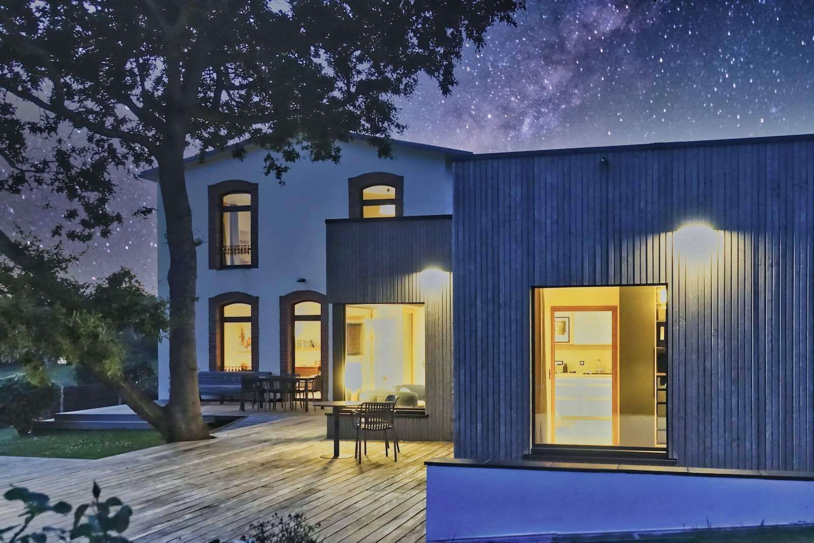 Ein modernes Haus mit einer Terrasse, einem Essbereich und einer durch die Fenster einsehbaren Küche.